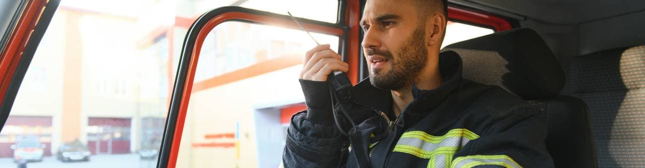 En brandman sitter i ett utryckningsfordon och använder en handradio.