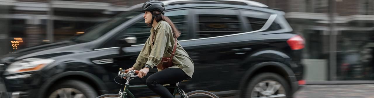 En svart bil åker på en gata i stadsmiljö jämte en cyklist.