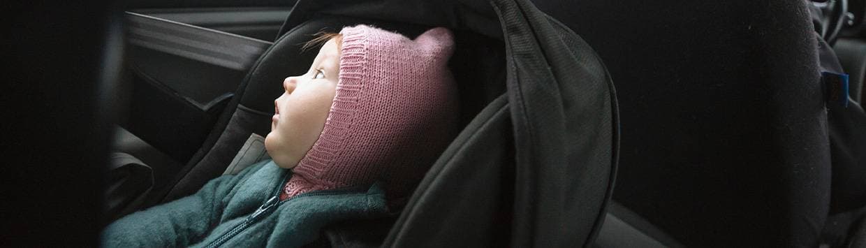 bebis sitter i bilbarnstol i baksäte på bil och tittar upp mot fönster