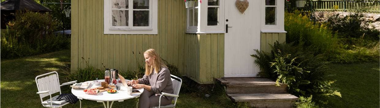 En kvinna sitter vid en dator utanför ett  grönt sommarhus.