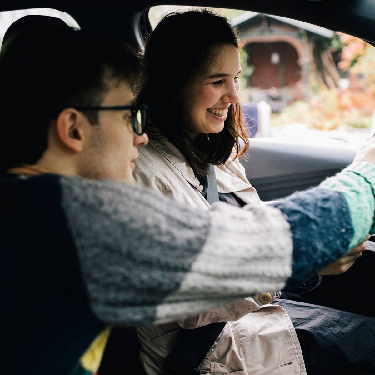 En tjej och en kille sitter redo att starta bilen och skrattar tillsammans.