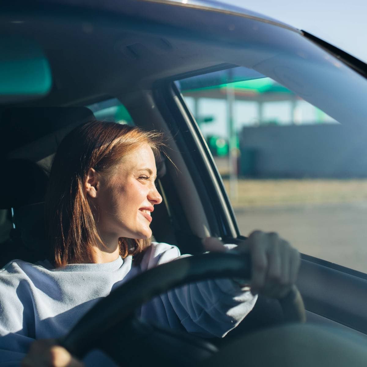 En kvinna sitter på förarplatsen i en personbil och tittar ut genom sidorutan.