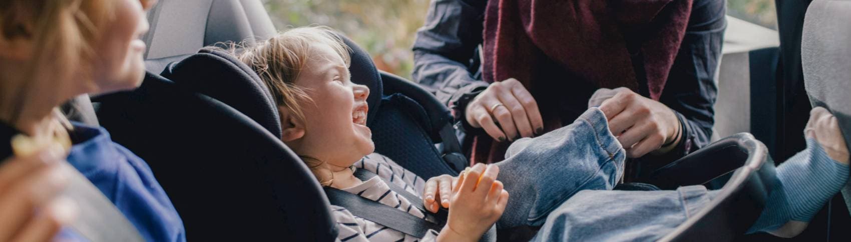 Ett barn sitter i bilbarnstol och skrattar.