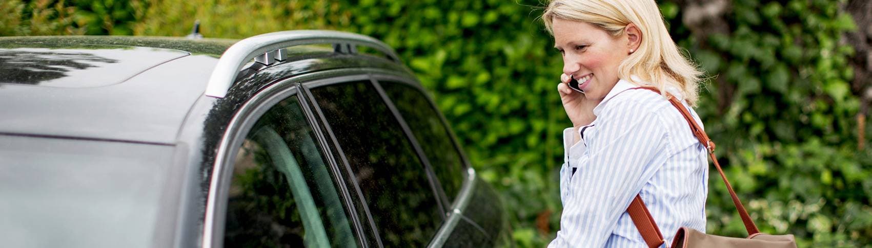 Kvinna pratar i telefon bredvid en bil