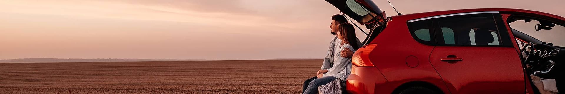 Par sitter i sin bil vid en åker och blickar bort mot horisonten.