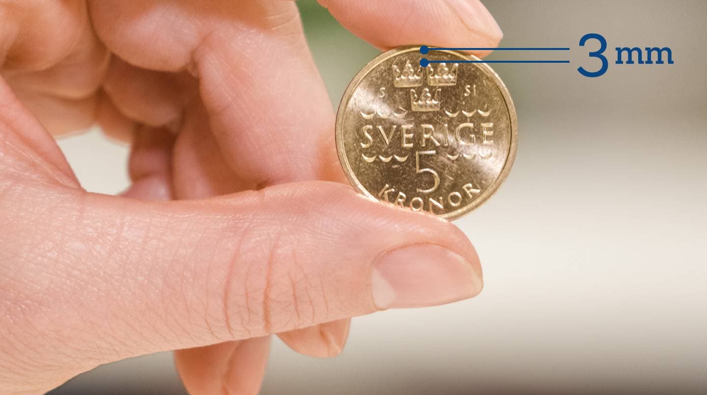Hand som håller upp en femkrona för att förklara att du kan mäta mönsterdjupet med hjälp av ett mynt.