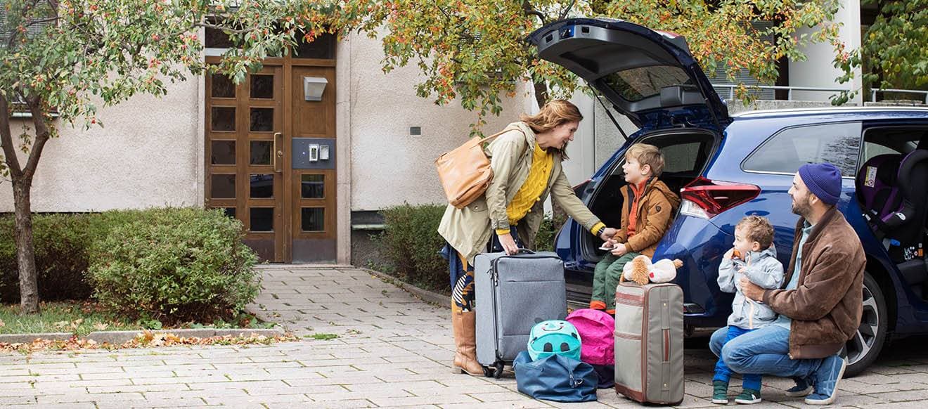 En familj med resväskor vid sin bil.