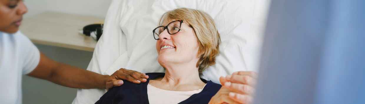 Vårdpersonal assisterar patient i sjukhussäng.