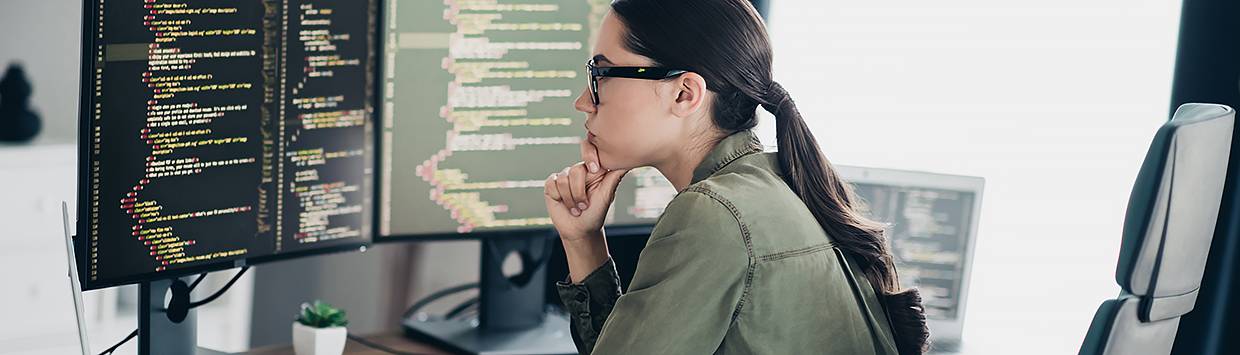 Kvinna sitter vid ett skrivbord, framför ett par monitorer.