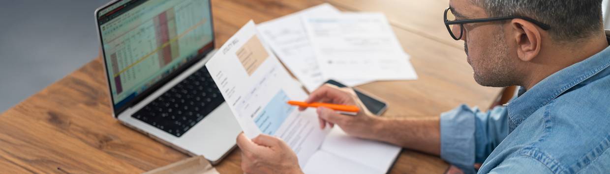 Man sitter vid datorn med viktiga papper och en penna.
