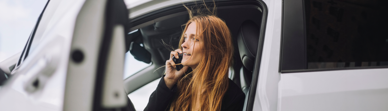 En kvinna sitter i en stillastående bil med öppen dörr och pratar i mobiltelefon.