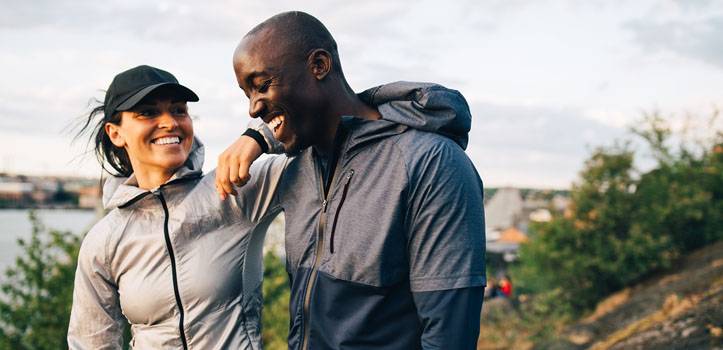 En leende kvinna och man st&aring;r i tr&auml;ningskl&auml;der ute i naturen