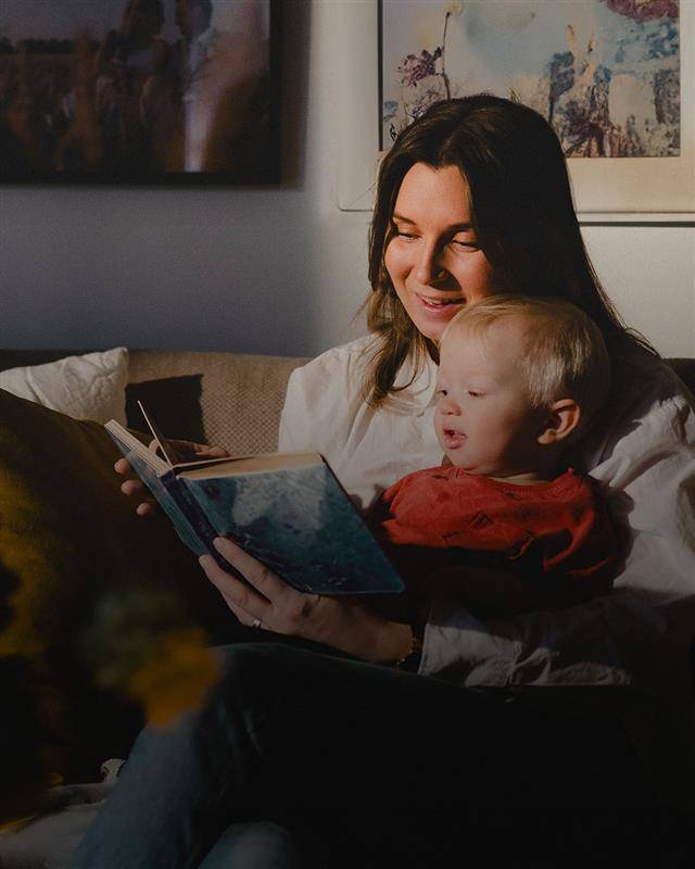 Kvinna sitter i en soffa med ett barn i knät och tittar i en bok tillsammans