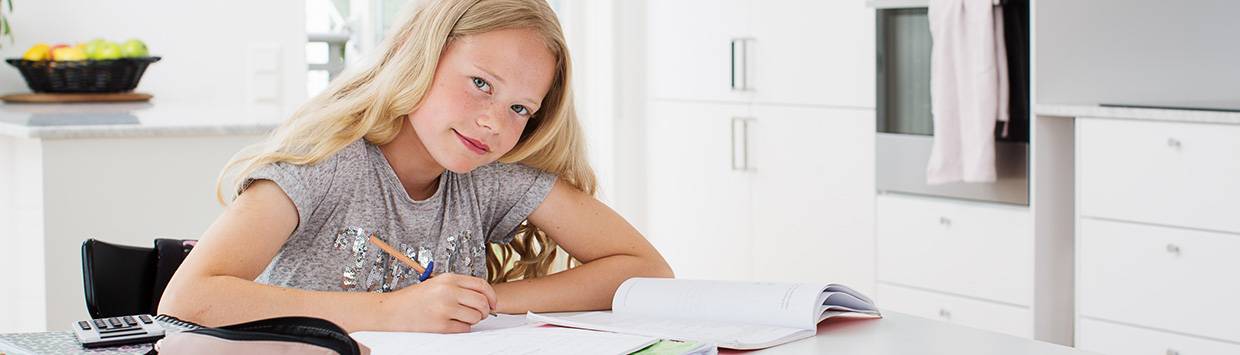 Flicka som sitter vid ett köksbord med skolböcker framför sig.