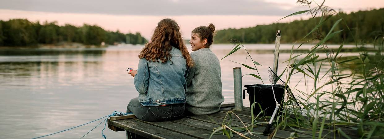 tv&aring; kvinnor sitter p&aring; en brygga vid vatten