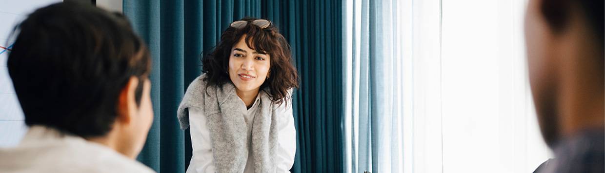 En kvinna st&aring;r lutad &ouml;ver ett bord och fokuserar p&aring; en m&auml;nniska i f&ouml;rgrunden