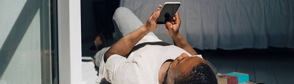 Kille som ligger p&aring; rygg p&aring; golvet och tittar p&aring; mobilen