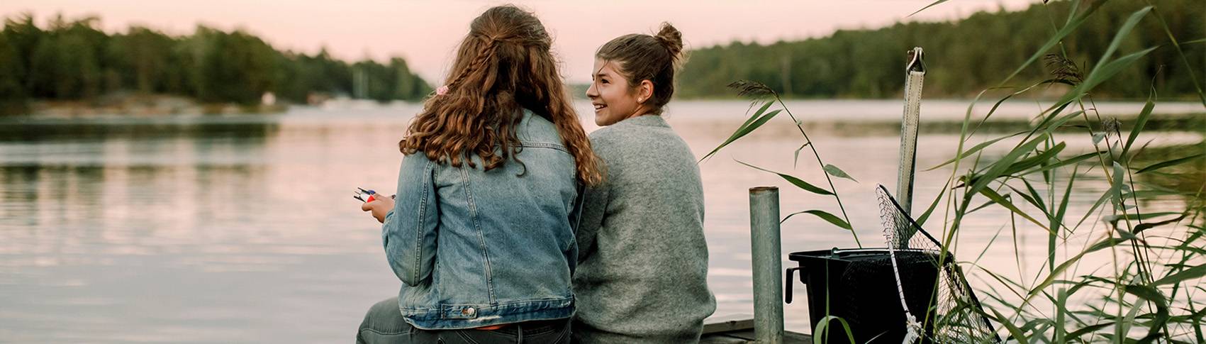 Tv&aring; tjejer sitter tillsammans p&aring; en brygga